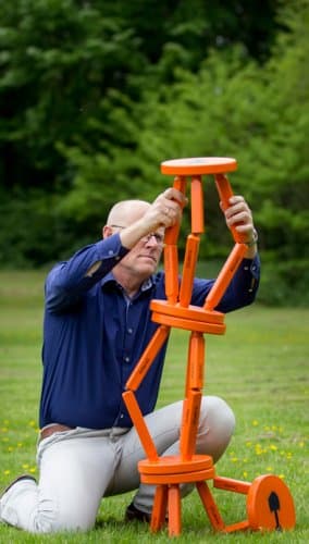 Een man bouwt op een grasveld een toren van oranje krukjes