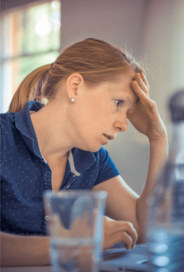 Een vrouw zit met haar hand tegen haar voorhoofd achter haar laptop